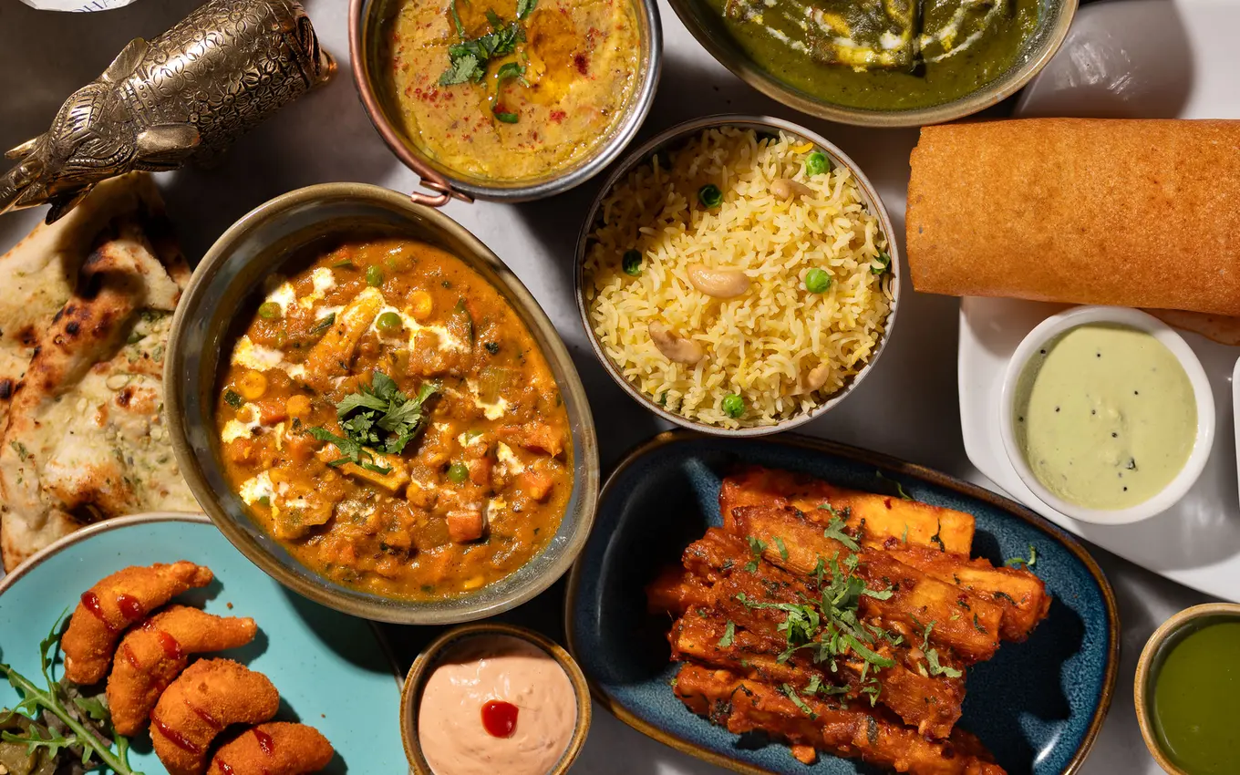 An overhead spread of Padharo dishes: paneer curry, dal, pilau rice, naan and a freshly rolled dosa