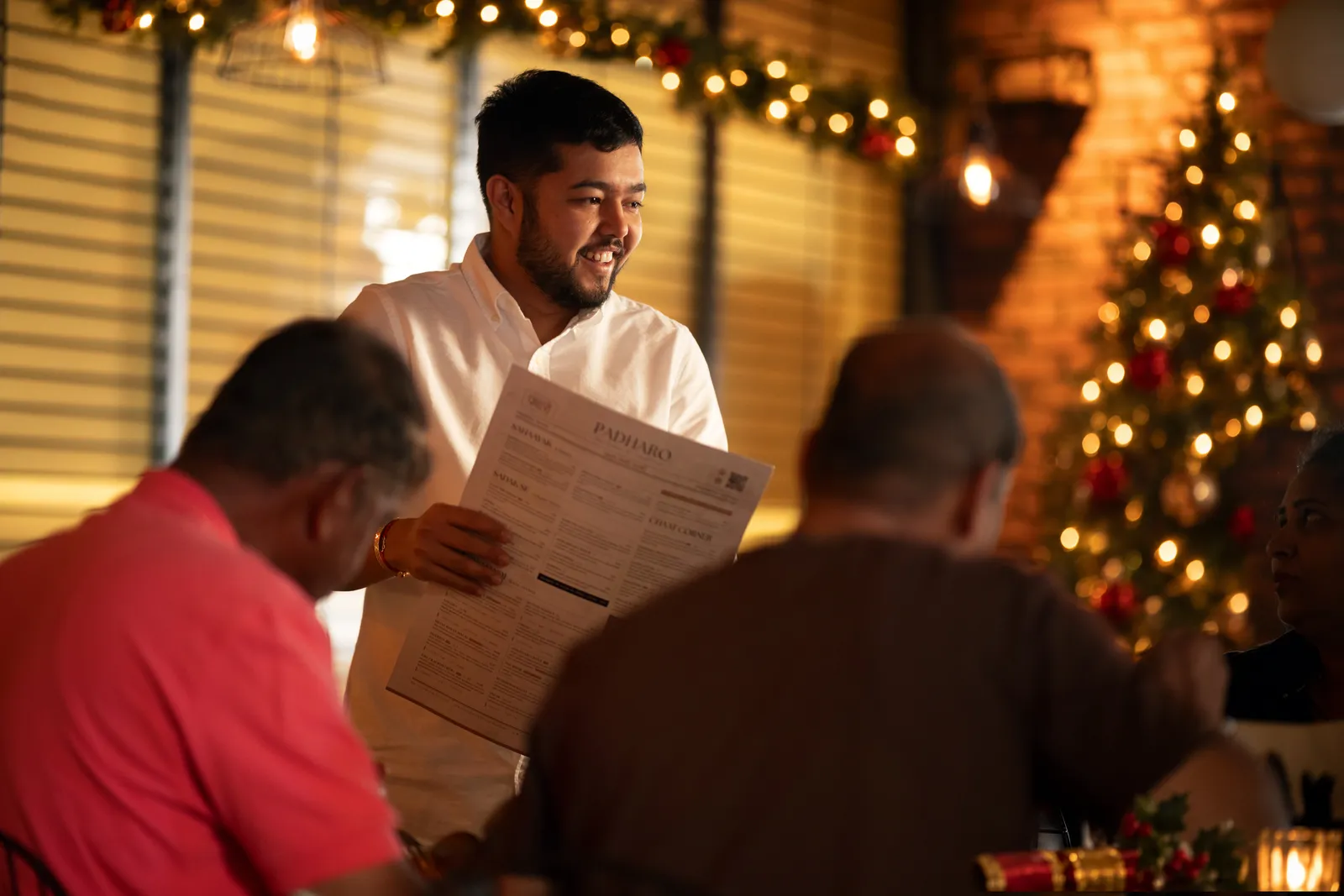 Ankit, Padharo's owner, taking a table through the menu, with the Christmas tree lit behind him