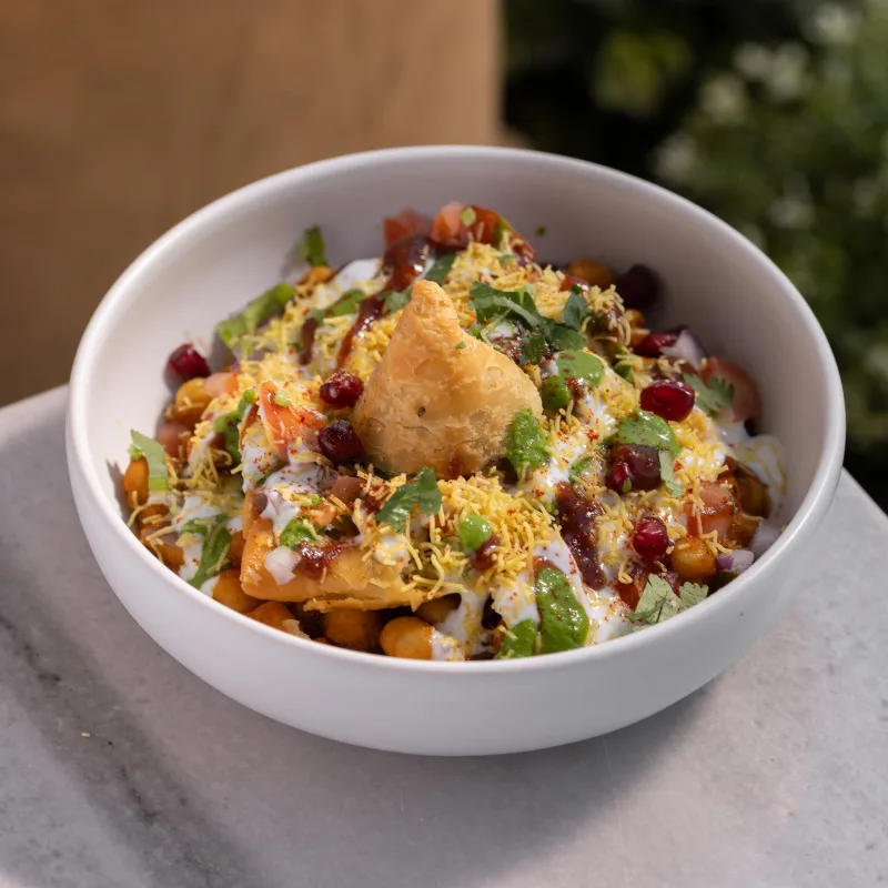 Samosa Chaat — A crisp samosa layered with chickpeas, yoghurt, tamarind and crunchy sev, vegetarian Indian dish at Padharo Southampton