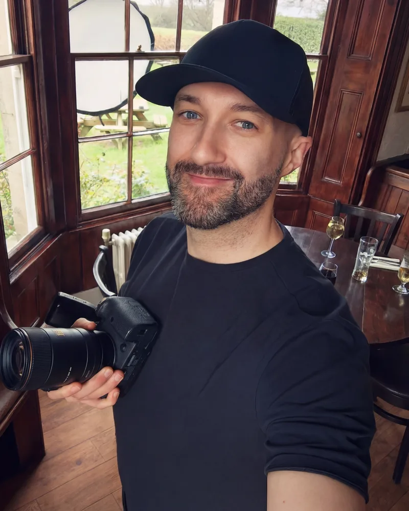 Ryan Stanikk, the commercial food and drink photographer who shoots Padharo, holding his camera on location in a restaurant dining room